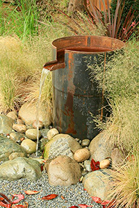 A steel container water feature while industrial in nature, softens the space with a constant noise of splash and movement. This is a pond-less feature minimizing maintenance.