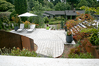 Eco-Prioria pavers were used to satisfy Mercer Island permeable surface requirements. Pavers were cut by hand to accommodate the curved steel edging line that is set into the paver patio grid. The steel edge line visually connects the steel panels in the landscape bed. Furniture-DWR, containers-Ragen & Associates.